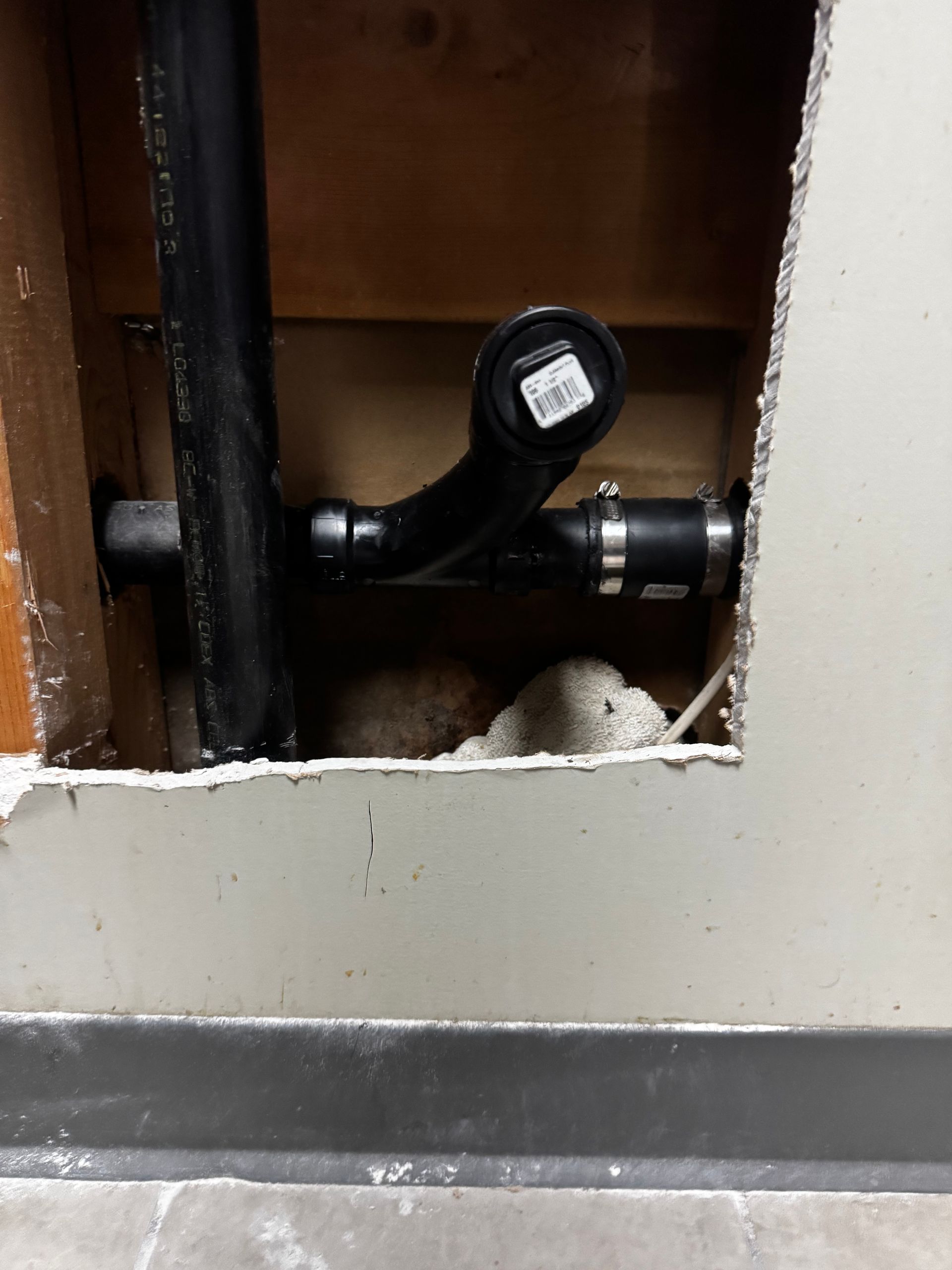 Black plumbing pipes in a wall opening, connected with a clamp.