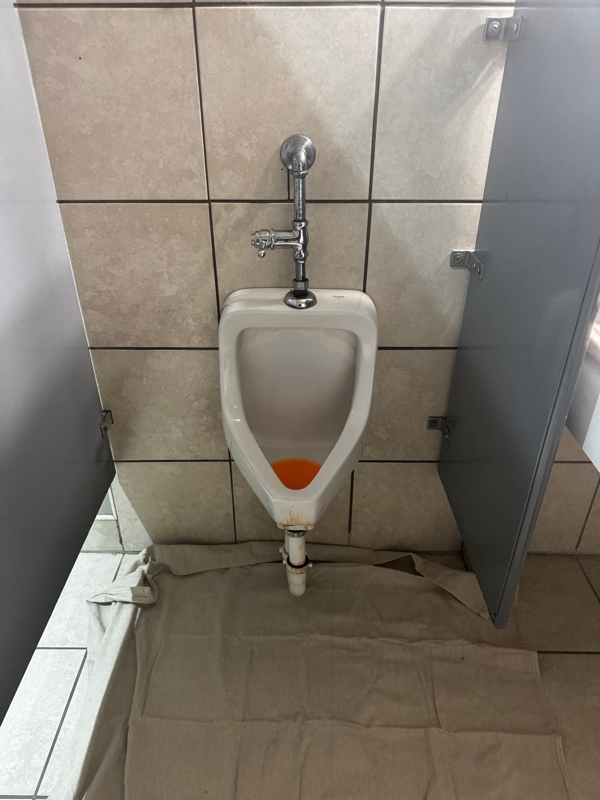 Urinal in public restroom with gray divider panels and tile background.