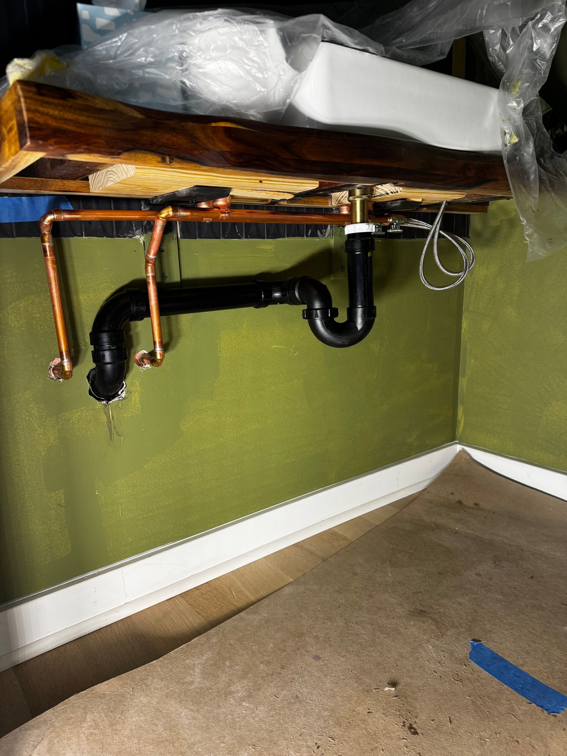 Plumbing under a sink. Copper pipes and black drainpipe against a green wall.