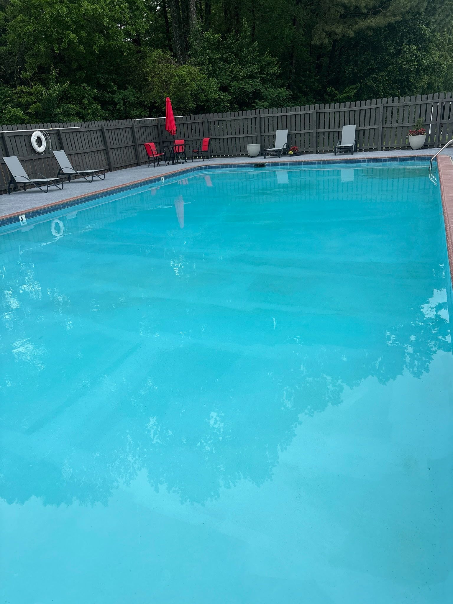 Outdoor swimming pool with clear blue water, lounge chairs, and trees in the background.