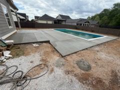 Backyard pool with unfinished concrete patio and exposed dirt beside suburban homes