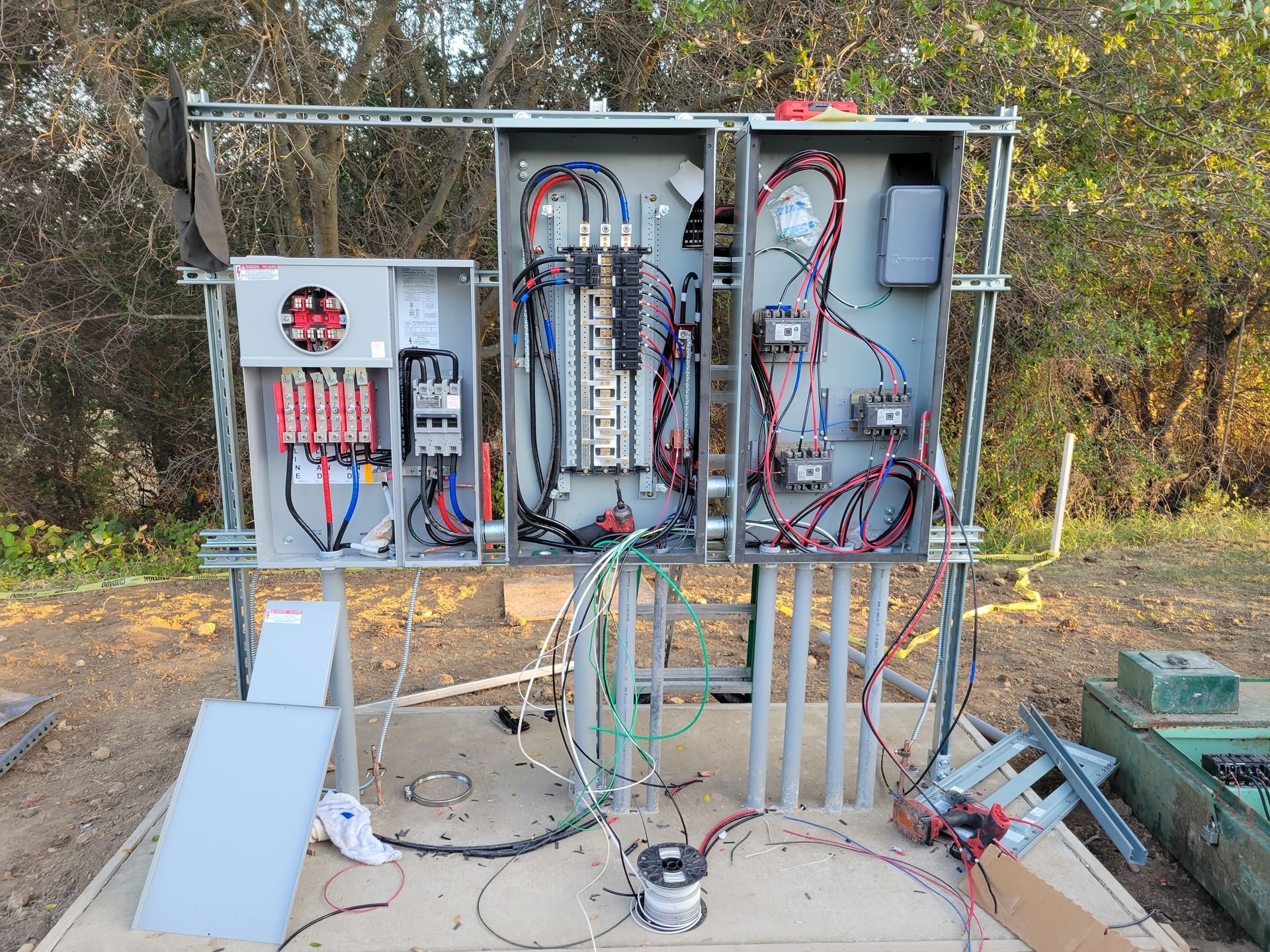 Outdoor electrical control cabinet with exposed wiring and panels on a metal frame in a wooded area
