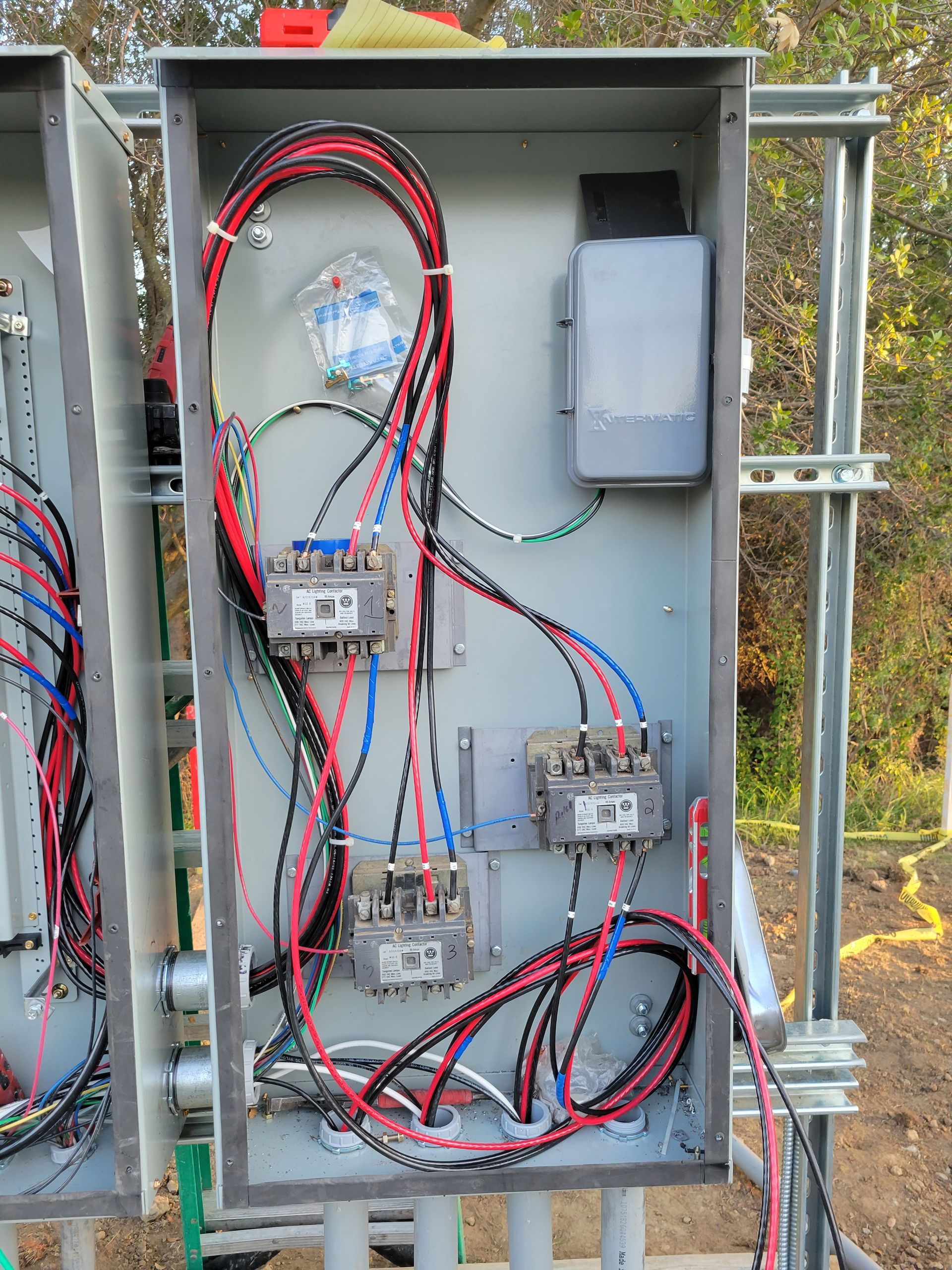 Open electrical control panel with red and black wiring, circuit modules, and gray enclosure outdoors