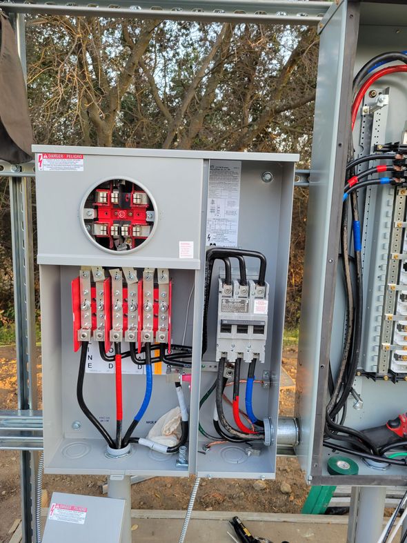 Electrical control panel with red breakers, gray wiring, and open metal enclosure outdoors.