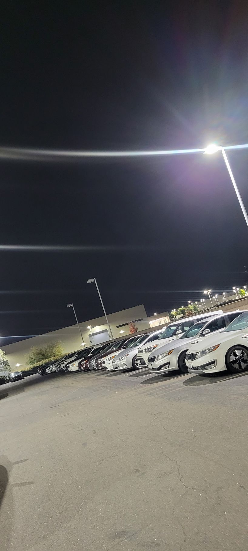Nighttime parking lot with rows of parked cars under bright streetlights, viewed at an angle
