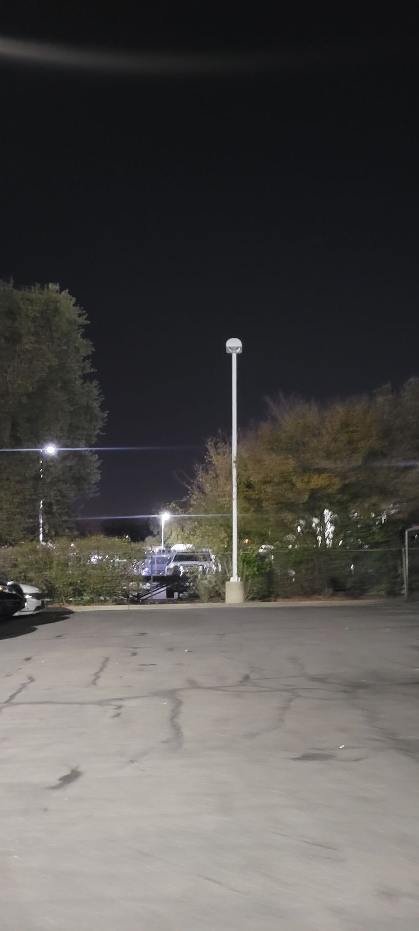 Empty parking lot at night with a lit streetlamp and trees along the road