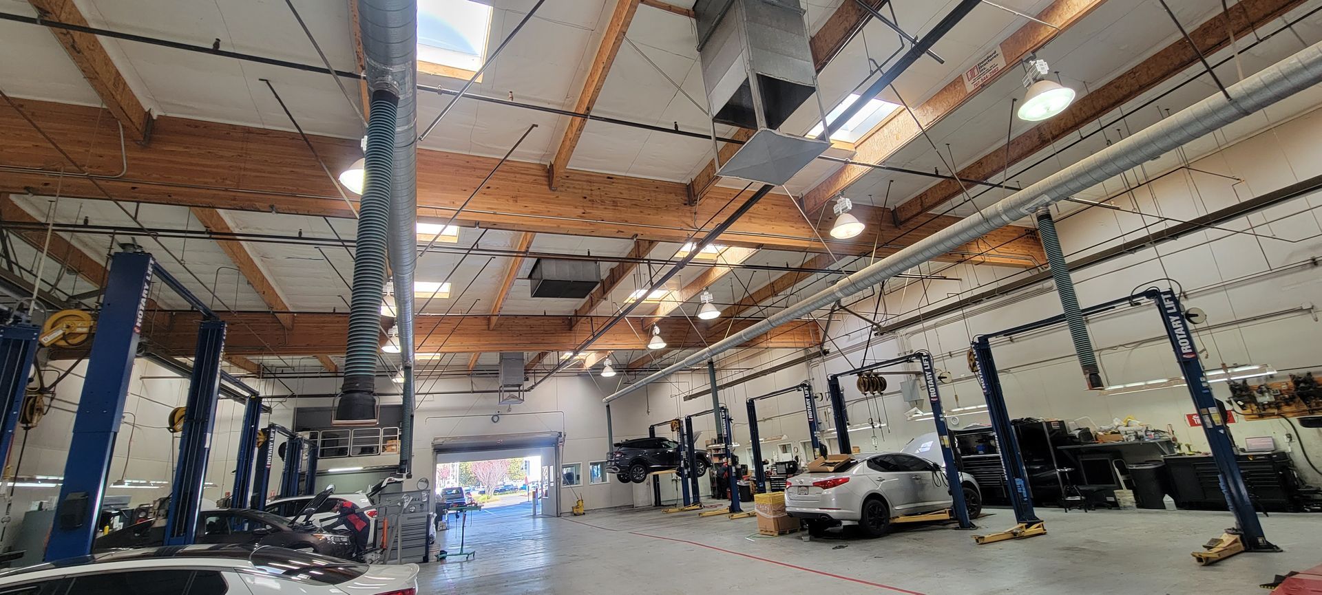 Wide-angle view of a car repair shop with vehicles on lifts and exposed ceiling beams