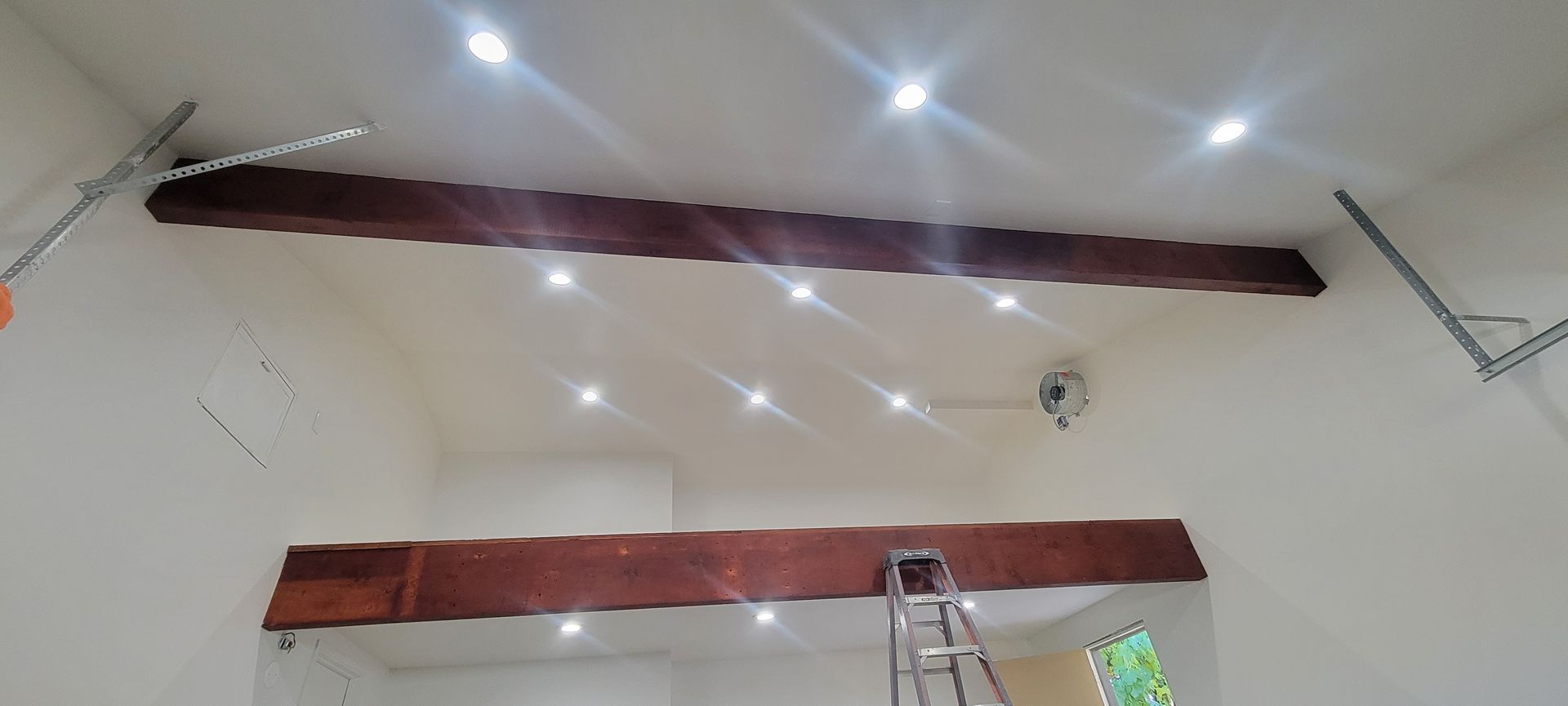 White ceiling with recessed lights, exposed beams, a ladder, and a security camera in a room under renovation