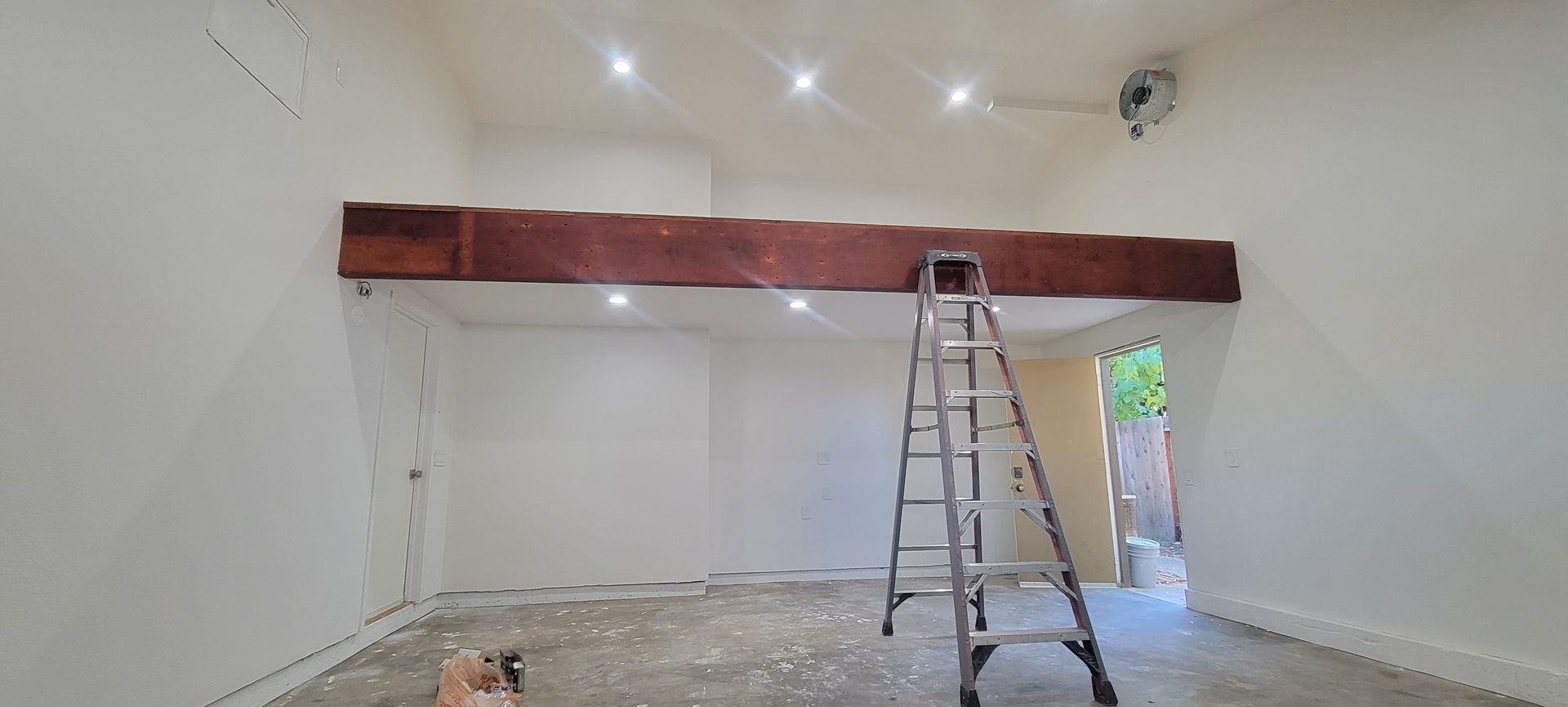 Renovated room with white walls, exposed wooden beam, ladder, and construction debris on the floor