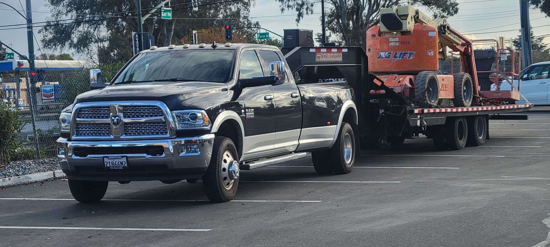 Black pickup truck hauling an orange utility trailer on a city street, side view.