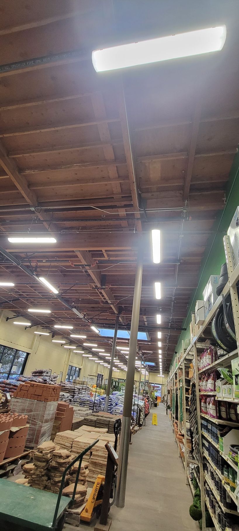 Warehouse aisle with tall shelves, stacked goods, and bright overhead lights under a high ceiling