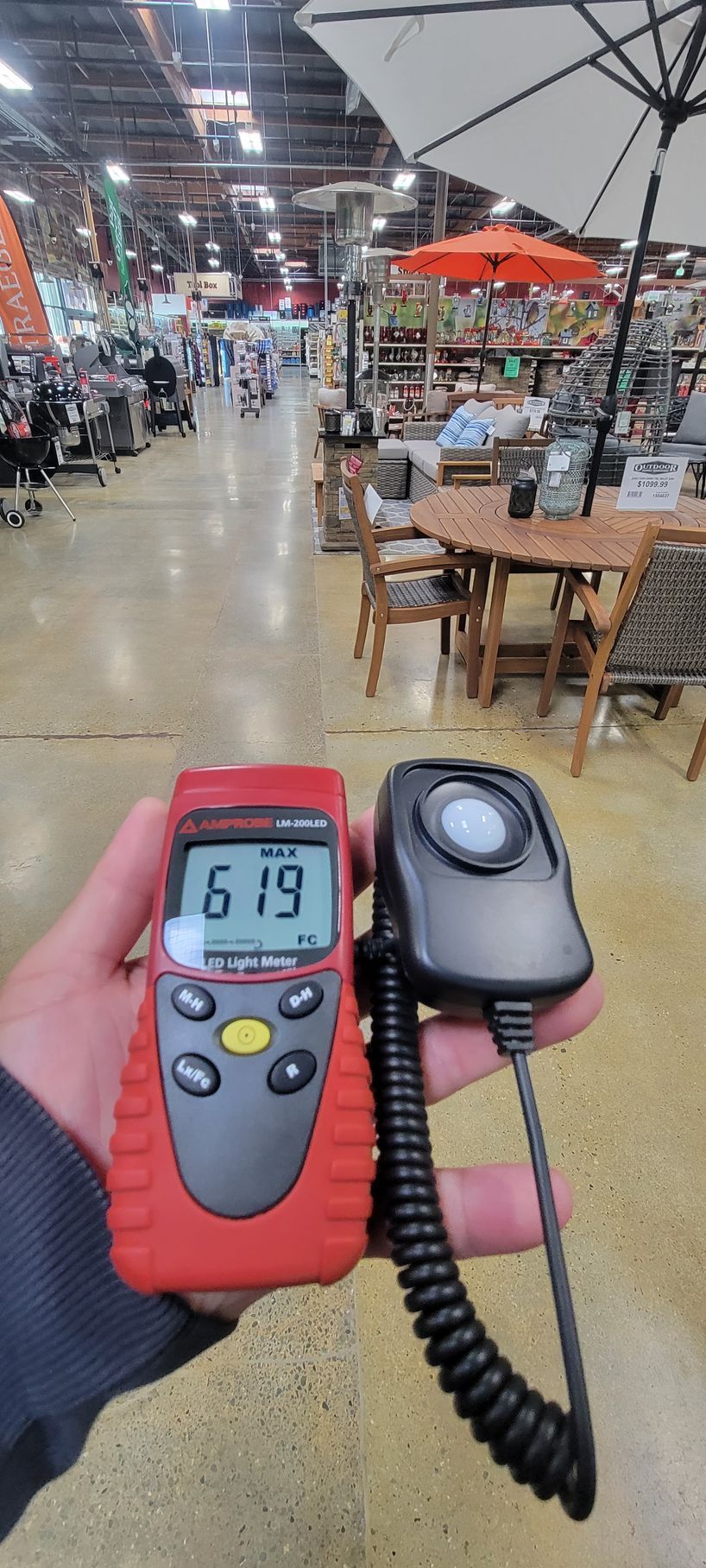 Handheld digital meter reading 61.9 in a large indoor warehouse or market aisle