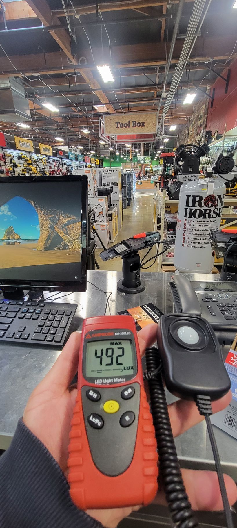 Red digital infrared thermometer on a store counter in a retail electronics aisle, reading 49.2°F.