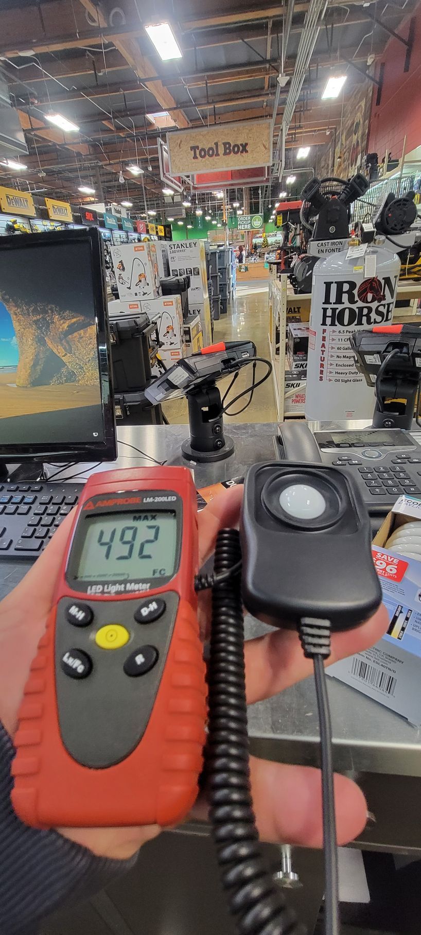 Hand holding an orange digital sound meter reading 49.2 dB in a busy retail store aisle
