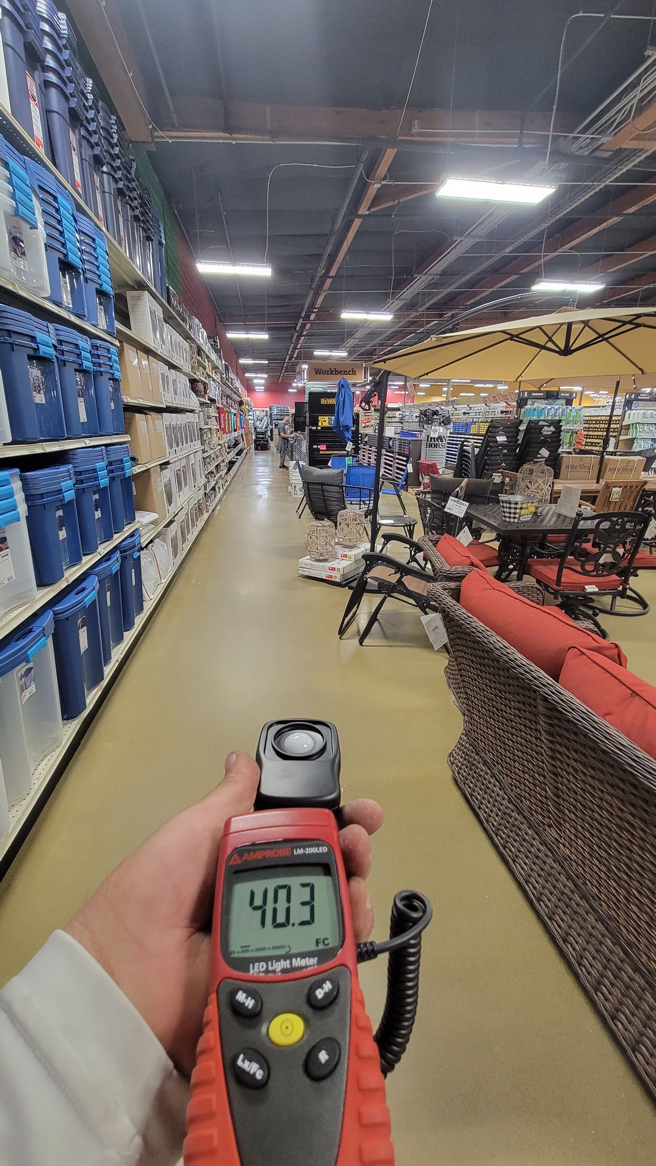 Person holding a meter in a store aisle with stacked boxes and racks of products.