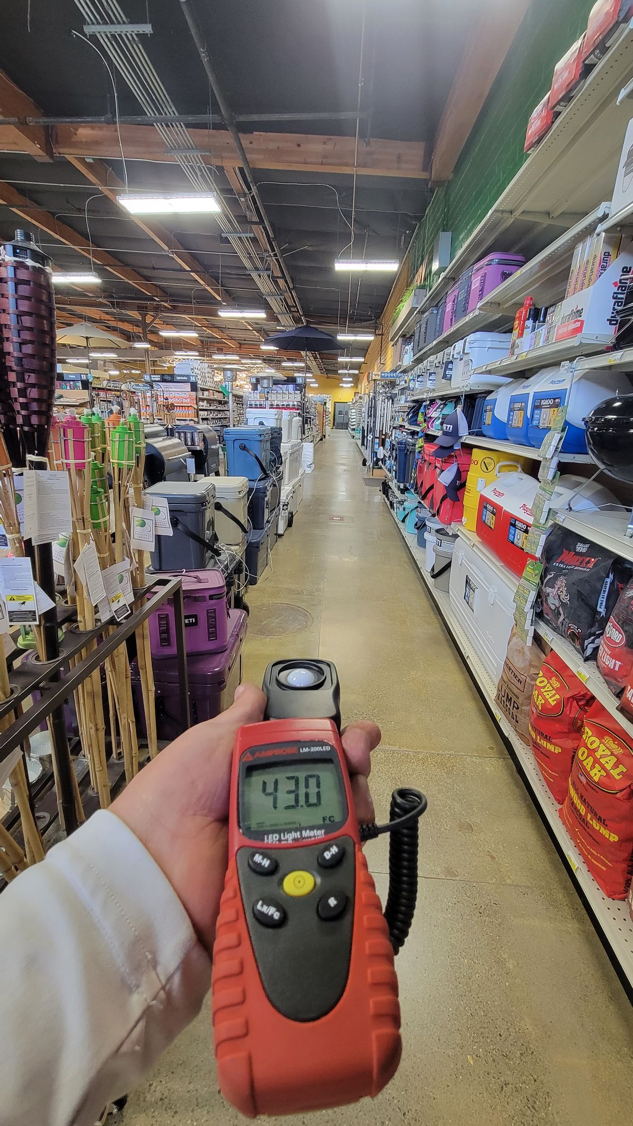 Hand holding a digital thermometer in a brightly lit grocery store aisle with stacked products on both sides