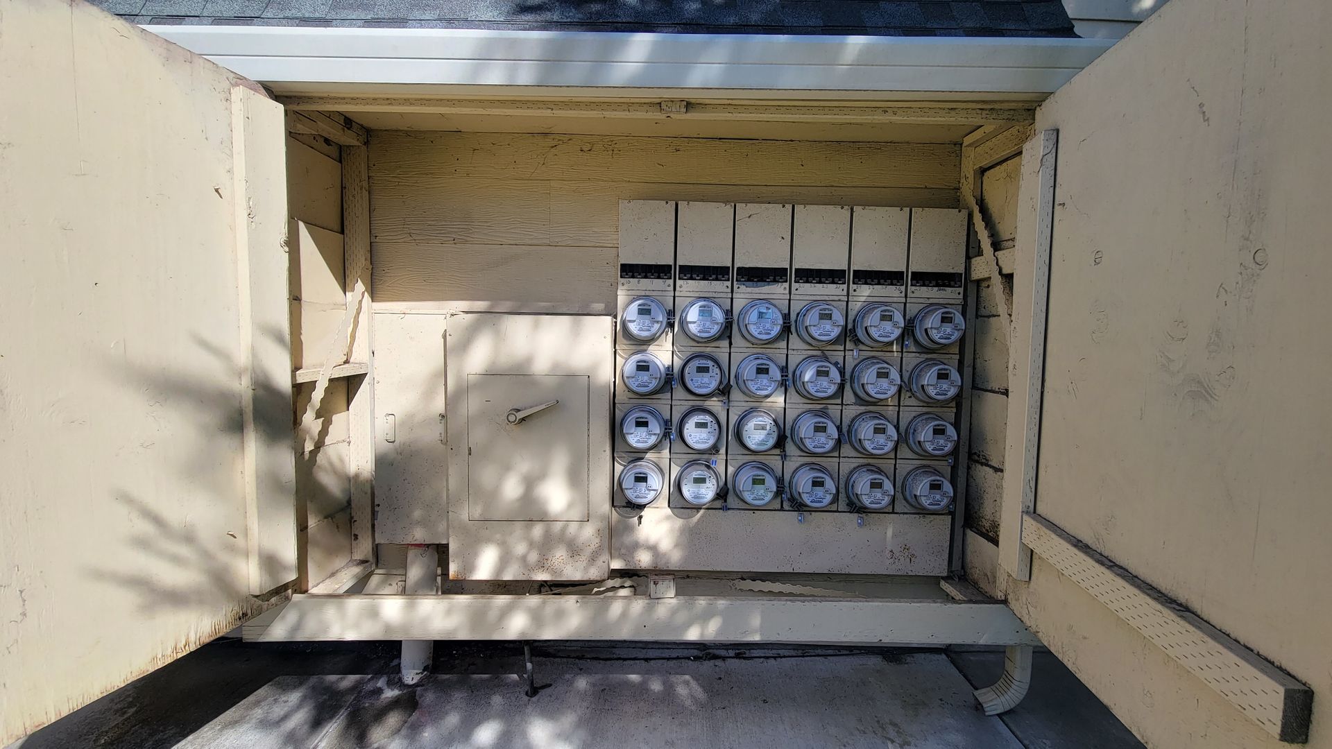 Open electrical meter box with multiple meters mounted inside a beige wall recess.
