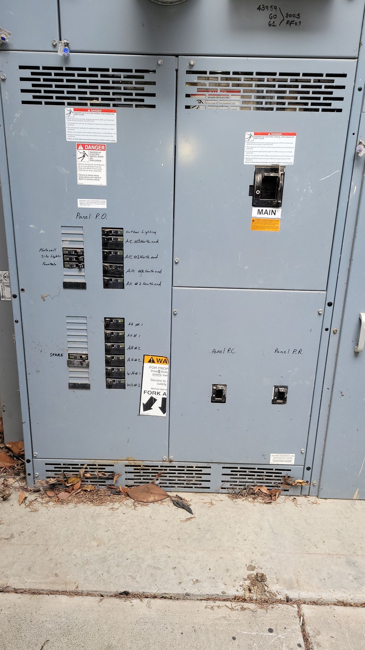 Gray electrical utility cabinet with warning labels and vents on a concrete sidewalk outdoors
