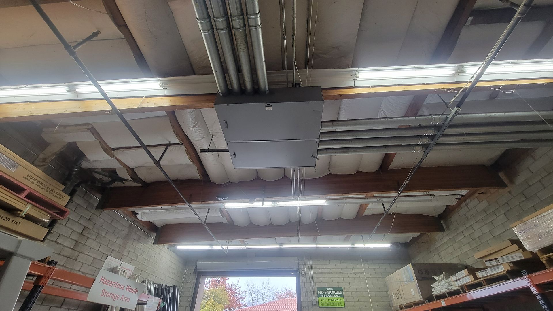 Interior of a warehouse with exposed ceiling beams, fluorescent lights, and stacked shelves along the walls.