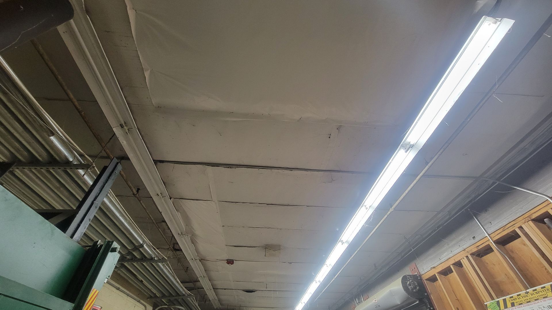 Warehouse ceiling with fluorescent strip lights, exposed beams, and wooden shelving along the right side.