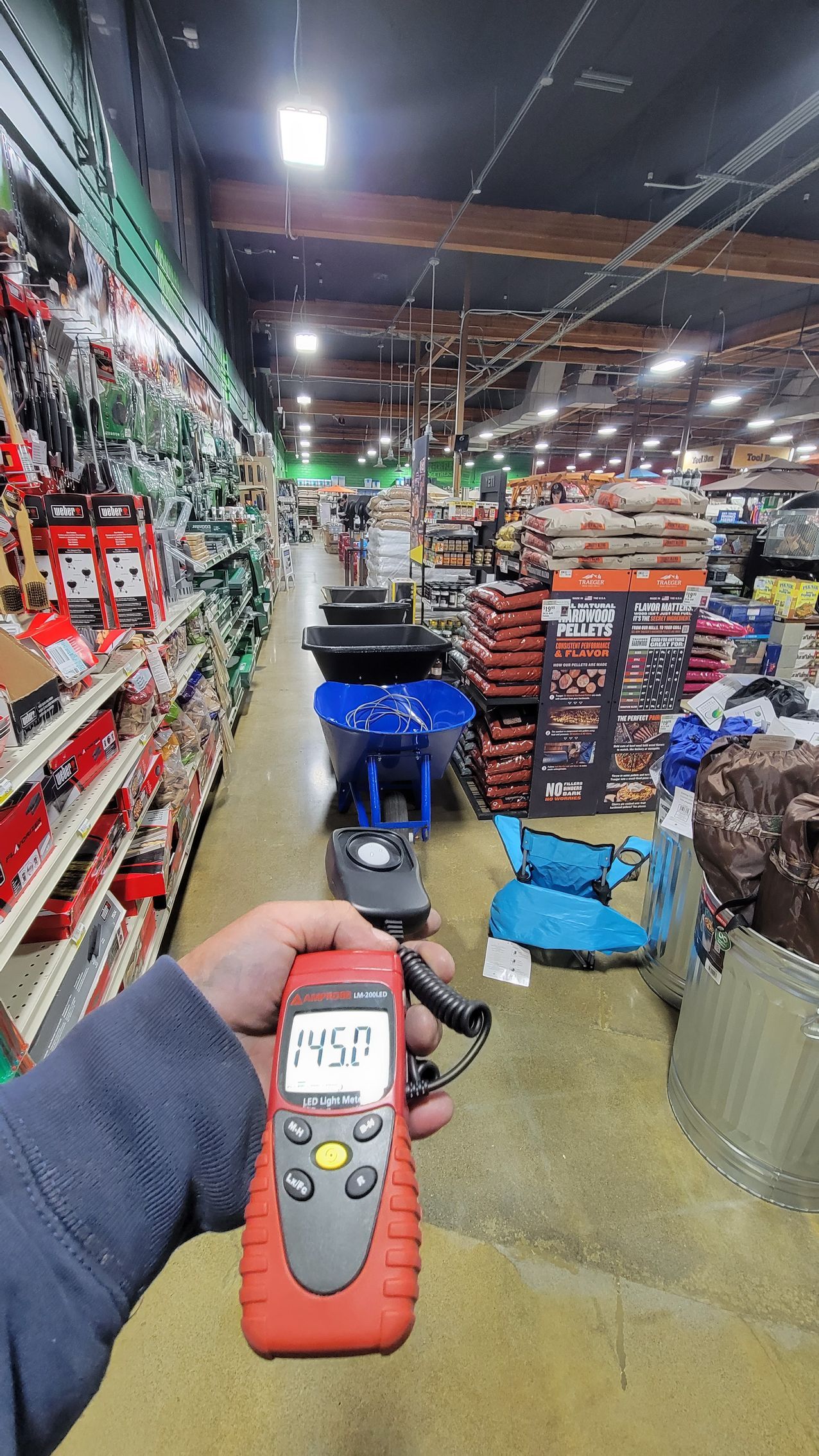A hand holds a red device in a warehouse aisle with stacked boxes and blue carts.
