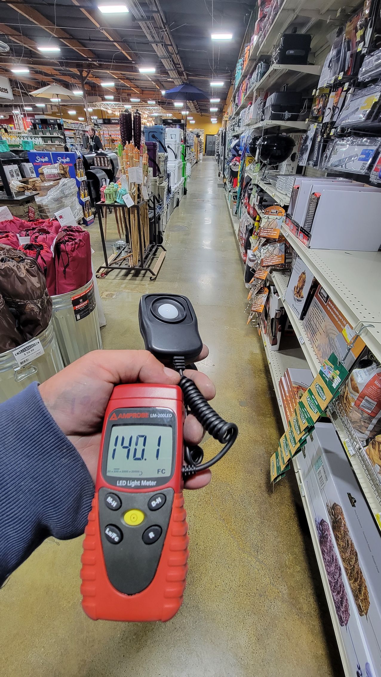 Handheld red meter showing 140.1 in a store aisle with shelves of assorted merchandise