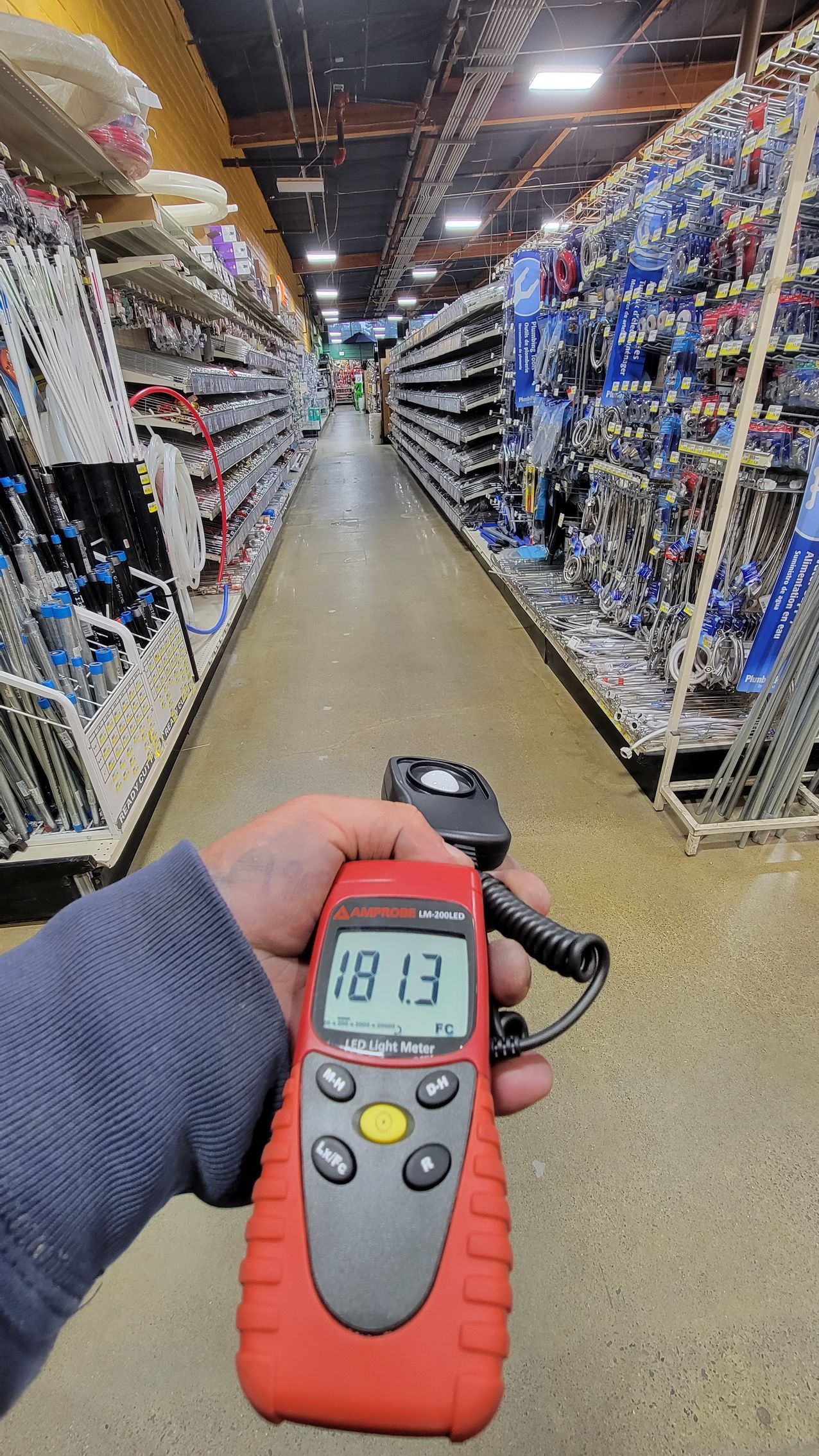 Handheld digital meter reading 18.3 in a store aisle with shelving on both sides.
