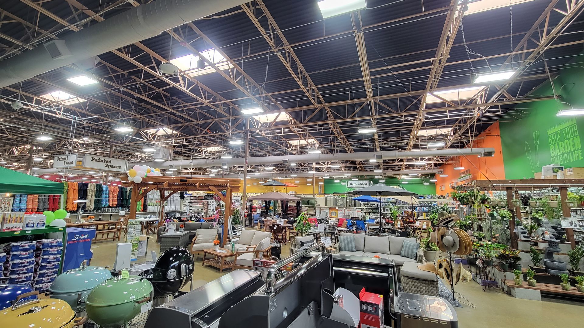 Wide-angle view of a brightly lit indoor market with shelves, tables, plants, and shoppers under a high ceiling
