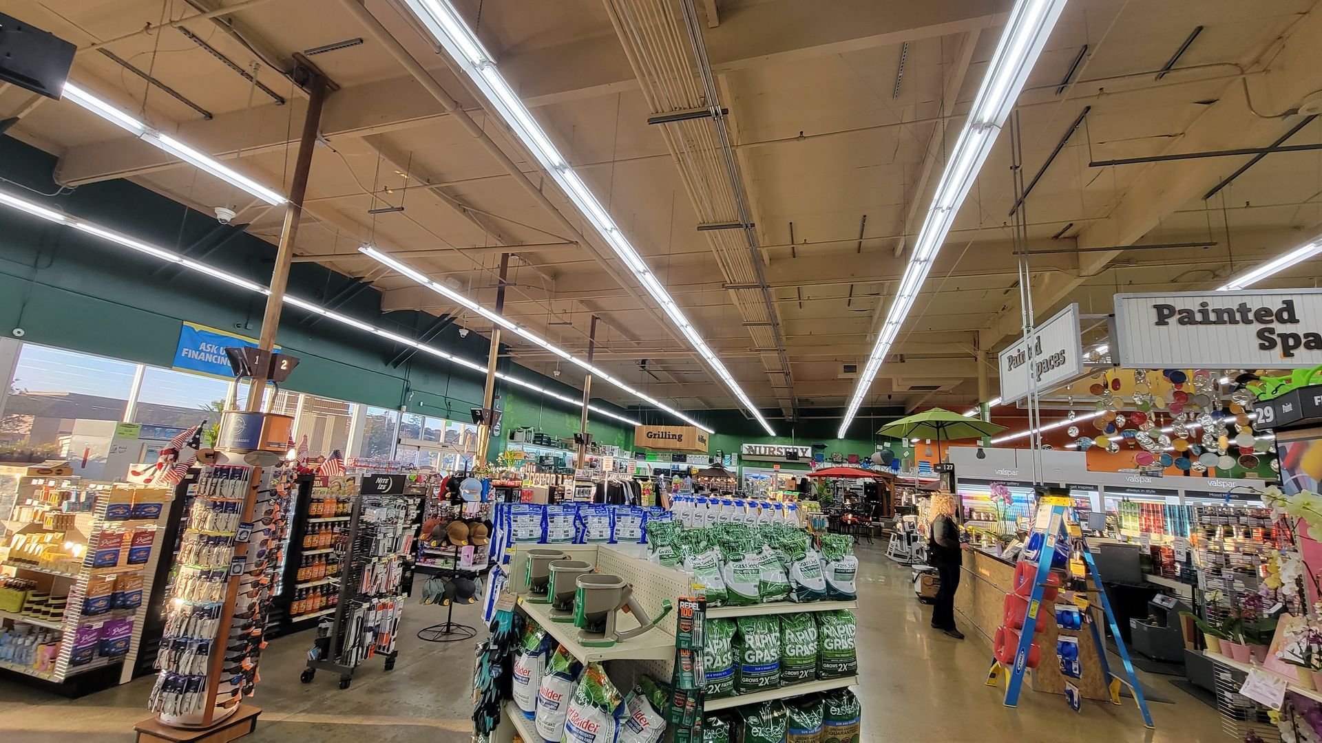 Wide grocery store aisle with bright ceiling lights and shelves of produce, snacks, and packaged goods