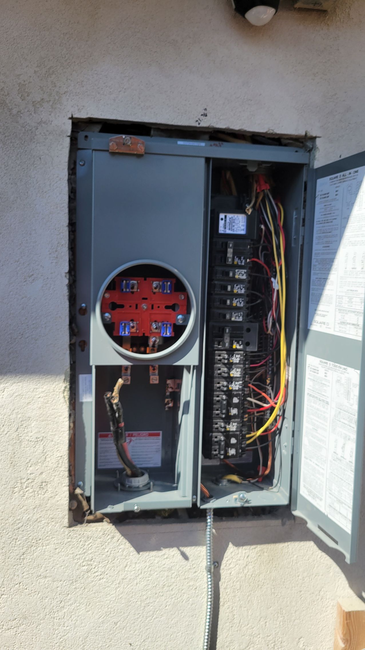 Open electrical panel cabinet with exposed wiring and meters on an exterior wall