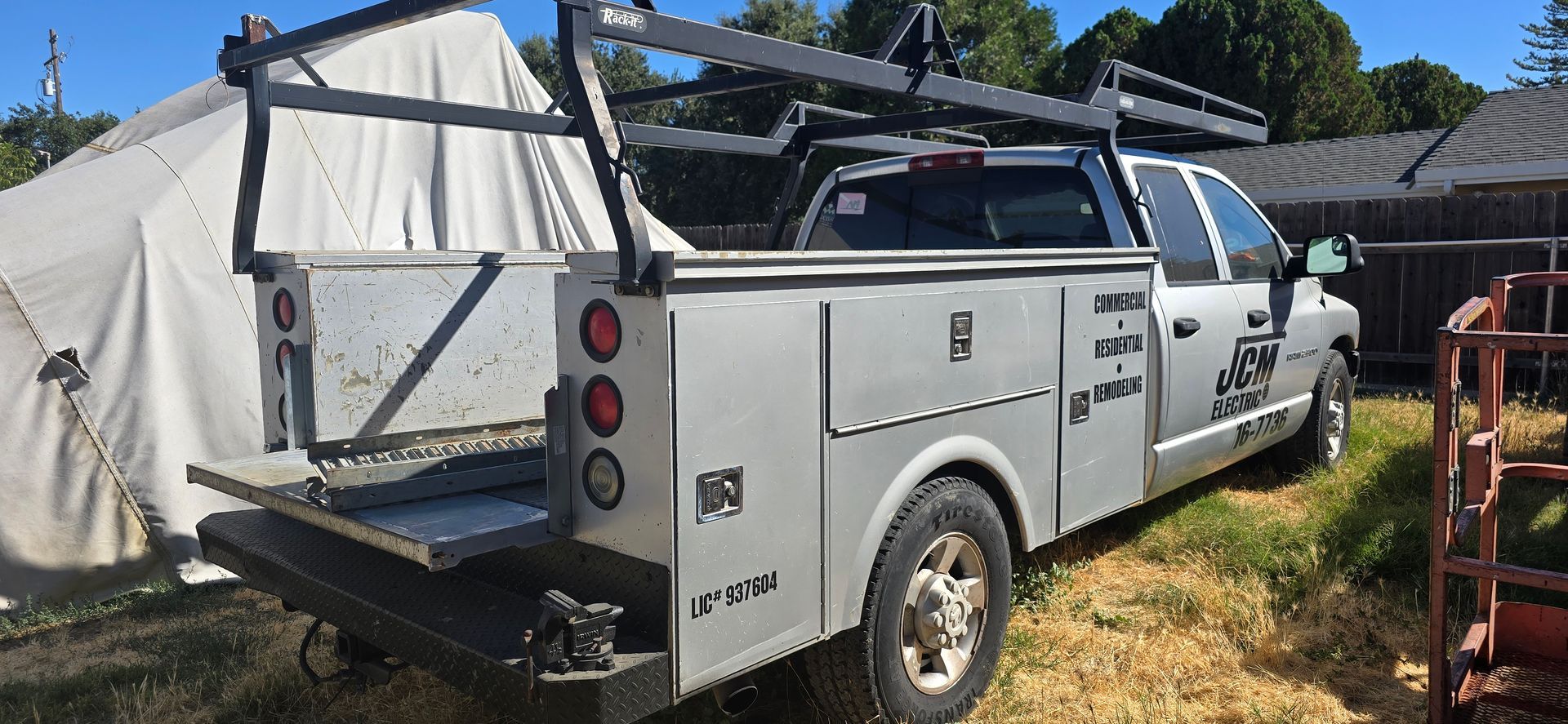 White utility truck with canopy parked beside a tarp-covered structure on a sunny grassy lot