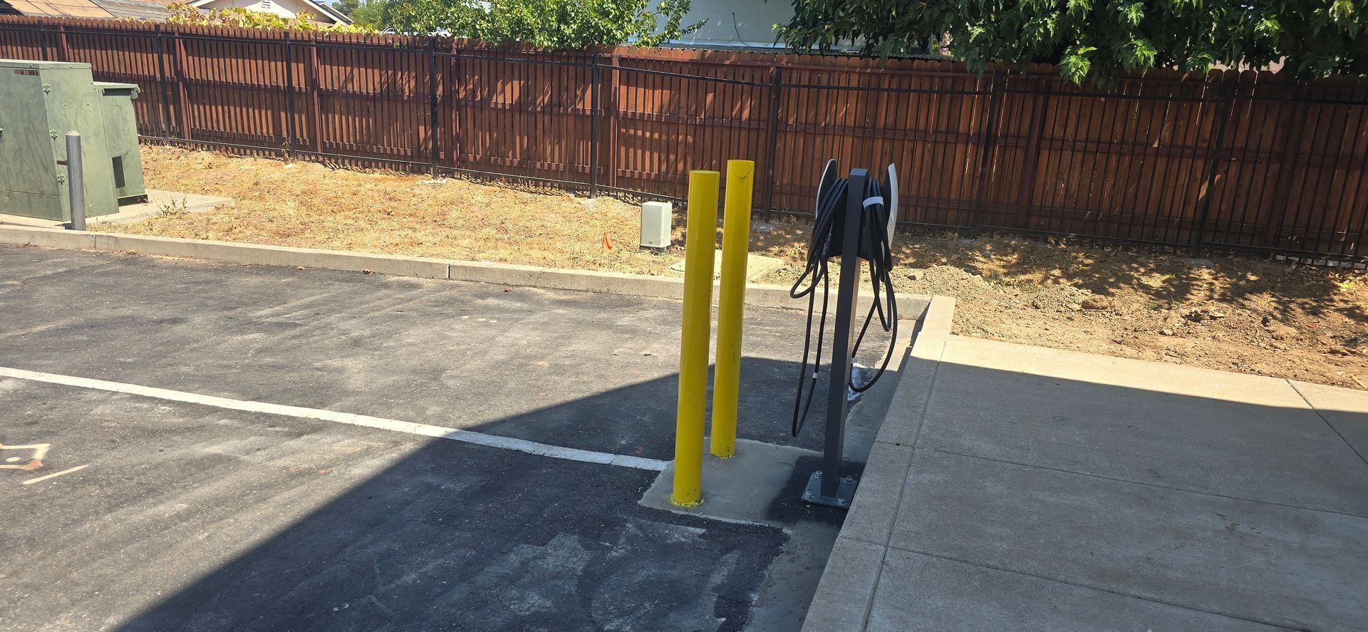 Outdoor sidewalk with yellow bollards and a bike rack beside a wooden fence in bright sun