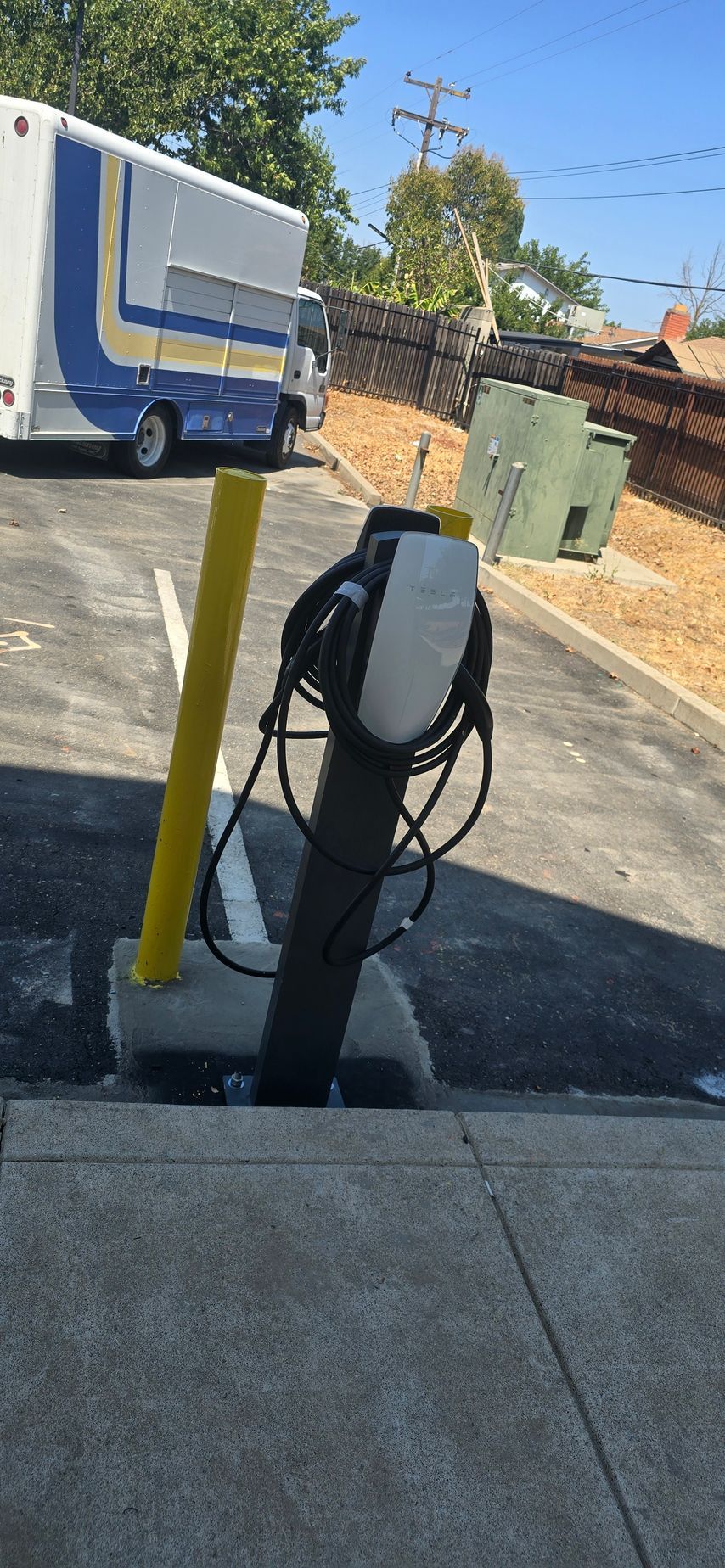 Parking lot EV charging station with a cable wrapped around a black post, beside a parked white truck.