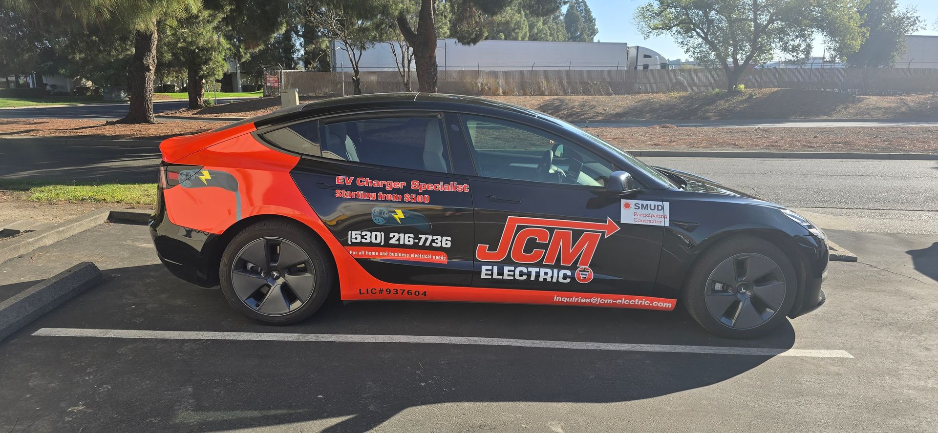 Red and black race car with decals parked on a road in a sunny outdoor setting
