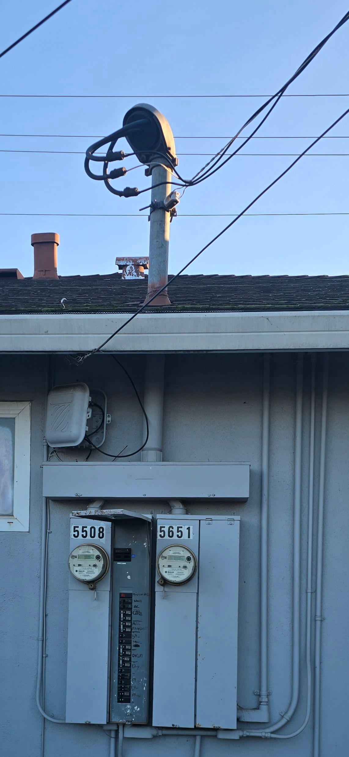 Utility meter and service pole on a house exterior with overhead power lines under a blue sky