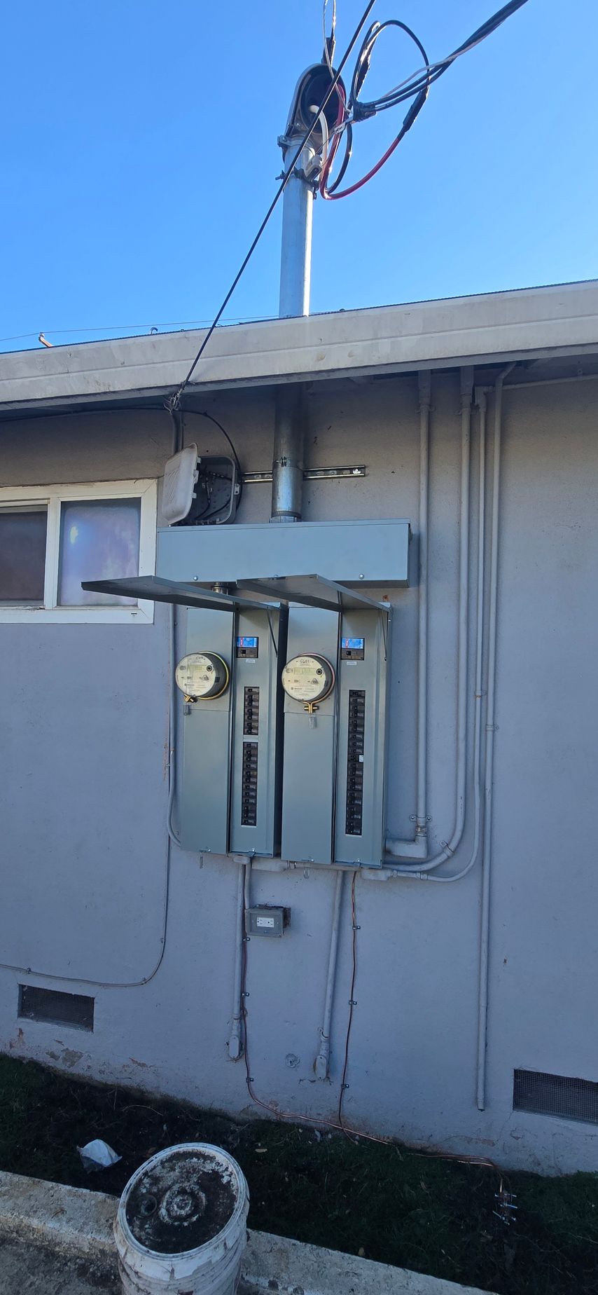 Damaged exterior electrical meter box mounted on a beige house wall, with exposed wires overhead.