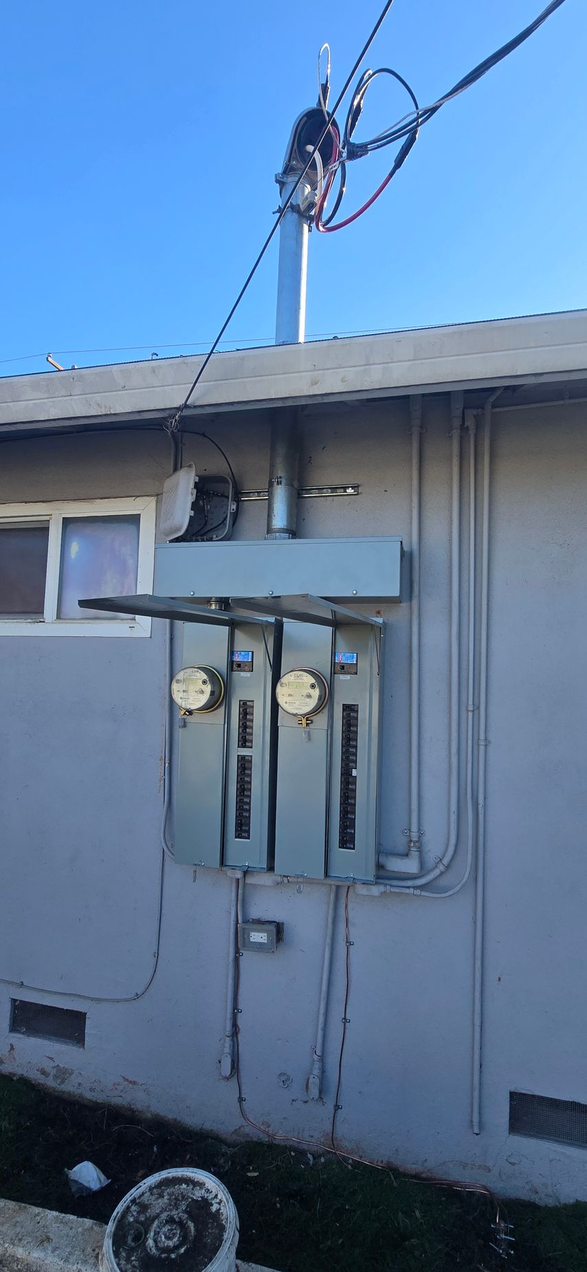 Wall-mounted utility meter and electrical box on a house exterior with overhead wires.
