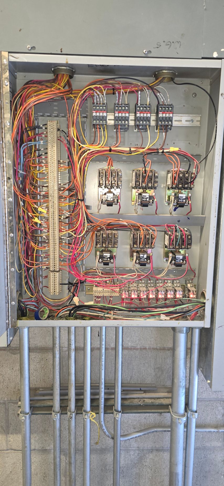 Open electrical panel with multicolored wiring and circuit components mounted on a wall.