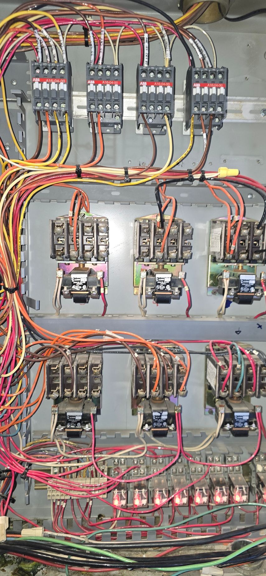 Electrical control panel with rows of relays, breakers, and dense red, yellow, and black wiring.
