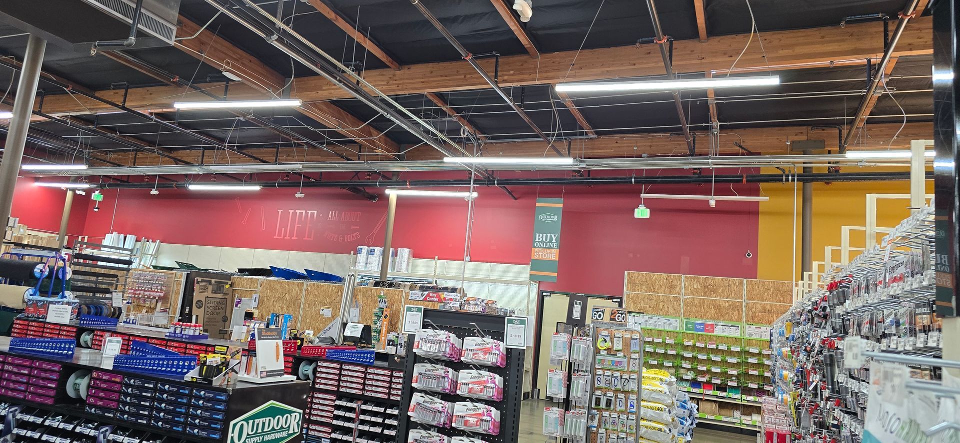 Grocery store aisle with shelves of packaged goods, produce, and red walls under exposed ceiling lights
