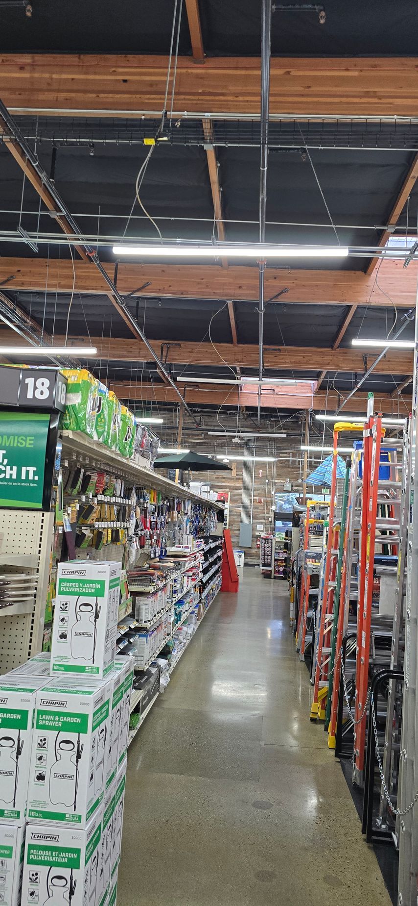 A warehouse store aisle with tall shelves of goods and overhead industrial lighting.