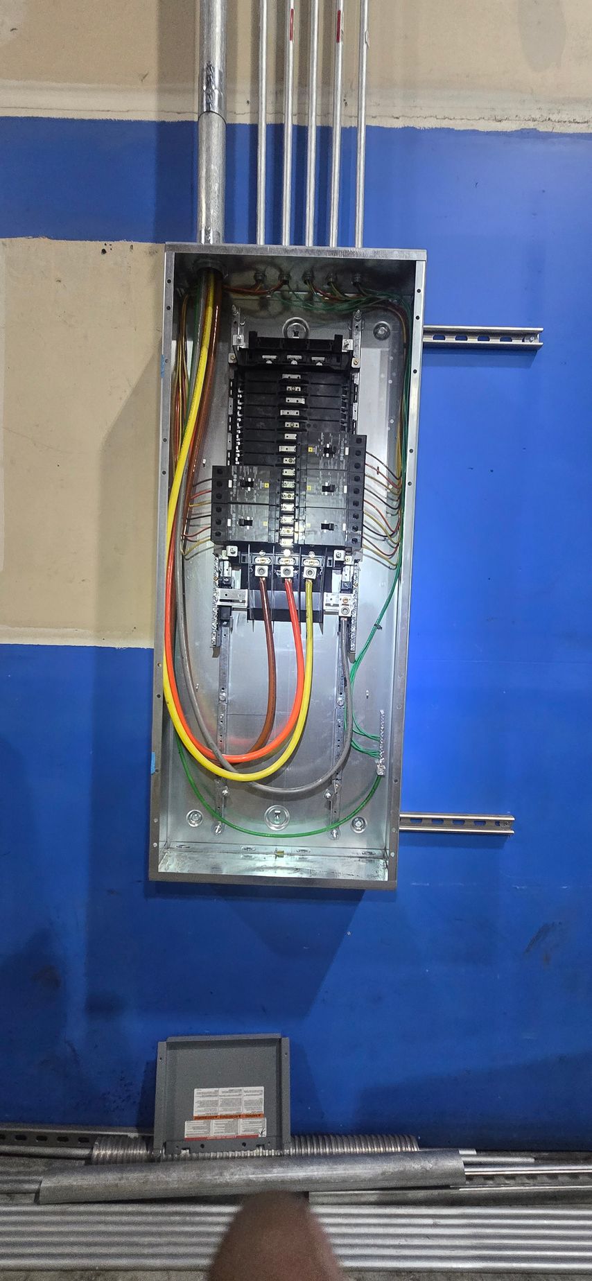 Open electrical breaker panel with exposed wiring and a blue wall background