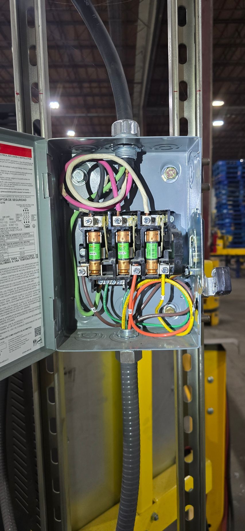 Open electrical control box with colored wiring and components mounted on a metal frame indoors