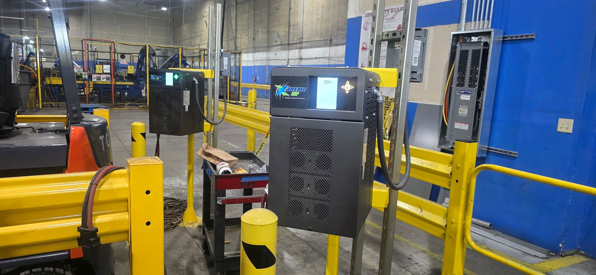 Industrial warehouse with yellow safety barriers and a conveyor machine in a blue-walled factory area