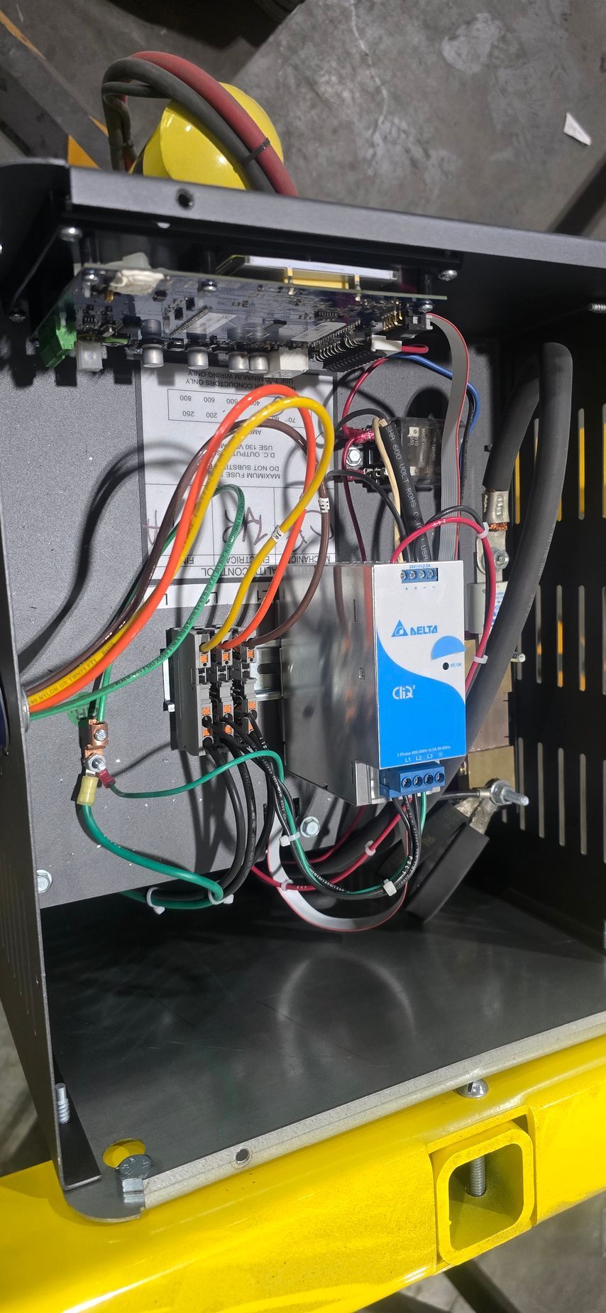 Open electrical enclosure with wires, connectors, and a blue circuit module mounted inside.