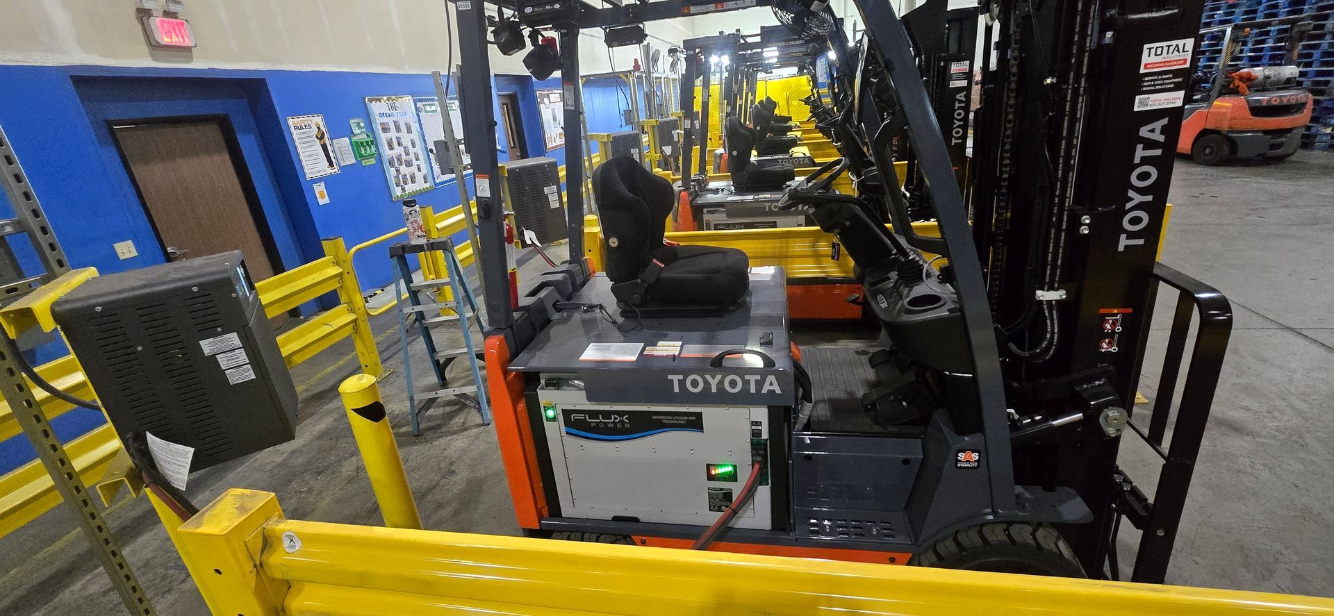 Toyota forklift in a warehouse aisle, with yellow safety rails and equipment in the background.