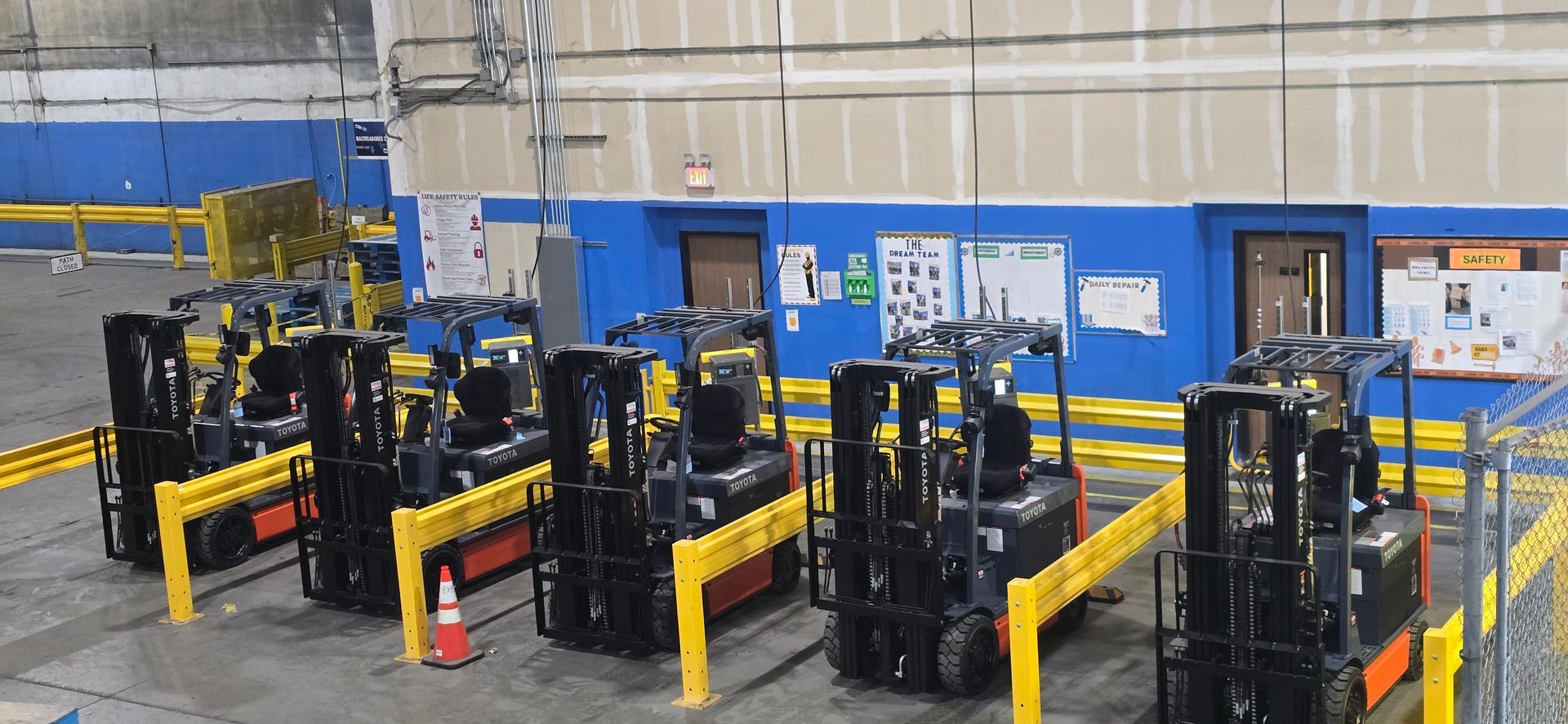 Warehouse with several black forklifts parked in rows behind yellow safety barriers