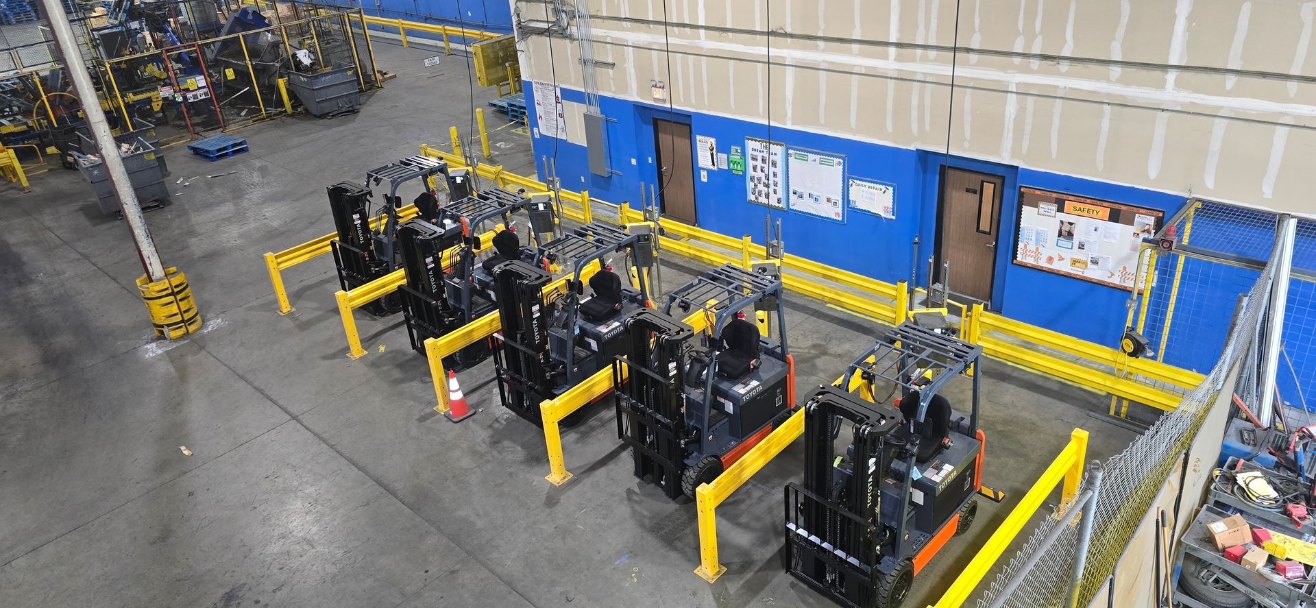 Warehouse with rows of black forklifts parked beside yellow safety barriers