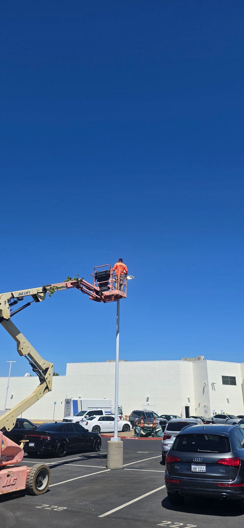 Worker in a bucket lift repairing a parking lot light against a clear blue sky.