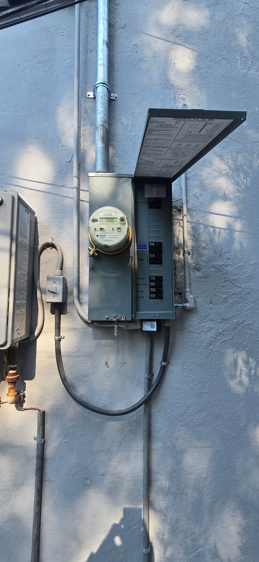 Open electrical meter and breaker box mounted on a gray exterior wall, door swung open.